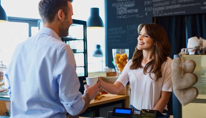 Young female barista serving coffee to customer in cafe